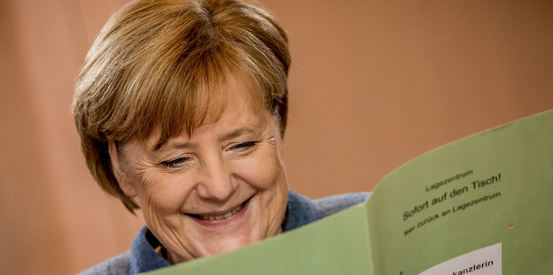 Angela Merkel schaut in Unterlagen und lacht