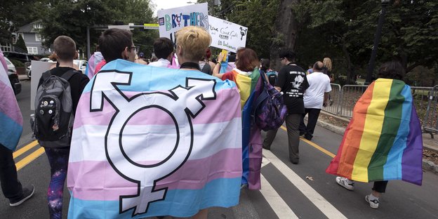 Demonstrant*innen halten eine Regenbogen- und All-Gender Flagge