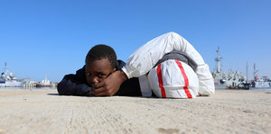 Zwei Flüchtlingskinder liegen auf dem Asphalt, nur von einem sieht man das Gesicht