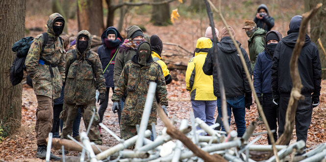 Mehrere vermummte Menschen stehen hinter einer Barrikade