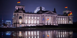 Das Berliner Reichstagsgebäude spiegelt sich am Abend beleuchtet in einer Pfütze
