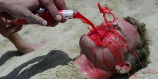 Jemand liegt am Strand und wird mit einem alkoholischen Getränk begossen