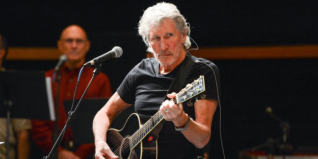 Ein älterer Mann mit grauen Haaren spielt Gitarre vor einem Mikrofon
