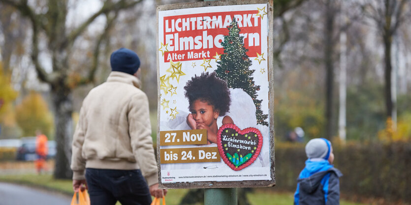 Werbeplakat für den Elmshorner Lichtermarkt an einem Pfahl, dahinter ein Mann mit Mütze und Plastiktüten