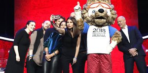 Eine Frau macht ein Selfie von sich - umgeben von mehreren Menschen und einem Maskottchen der WM 2018