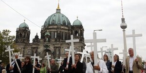 Im Vordergrund viele Menschen, die alle ein weißes Kreuz vor sich hertragen, im Hintergrund der Berliner Dom und der Fernsehturm