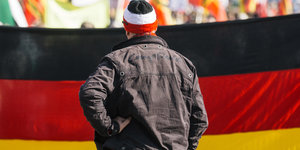 Ein Mann mit Strickmütze in den Nationalfarben des deutschen Reiches steht vor einer Deutschlandfahne