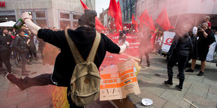 Bei einer Demo tritt ein vermummter Mann mit Bier in der Hand einen Gegenstand weg