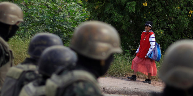 Eine bunt gekleidete Frau läuft an einer Gruppe Soldaten vorbei.