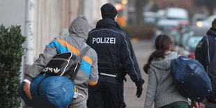 Zwei Polizisten führen zwei Personen zu einem Polizeiwagen