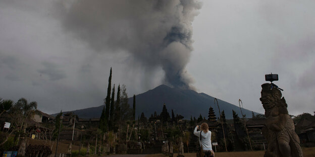 Ein rauchender Vulkan am Horizont, vorne fotografiert eine Frau