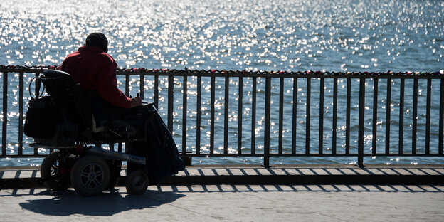 Eine Frau in einem Rollstuhl schaut von einer Promenade aufs Meer