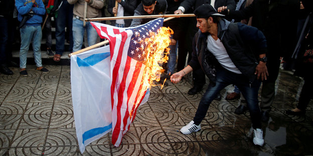 Menschen verbrennen auf einem Platz eine US-Flagge und eine israelische Flagge