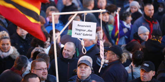 Zwischen Demonstranten ragt ein hölzerner Galgen empor. An ihm hängt ein Zettel „Reserviert Sigmar ,Das Pack` Gabriel“