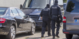 Zwei Polizisten laufen zwischen zwei Autos umher