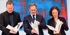 Klaus Lederer von der Linken, Michael Müller von der SPD und Ramona Pop von den Grünen schauen in je ein Exemplar des Koalitionsvertrags