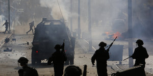Silhouetten von Soldaten und anderen Menschen sind zwischen Rauchschwaden und Panzer auf einer Straße sichtbar