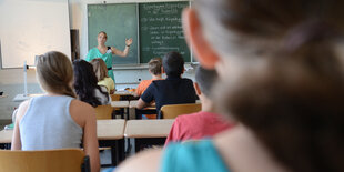 Eine Lehrerin steht an der Tafel und wendet sich ihrer Klasse zu