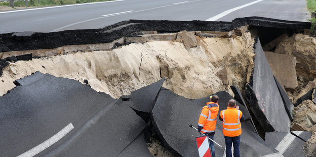 Zwei Menschen in Warnwesten stehen an der eingestürzten Autobahn