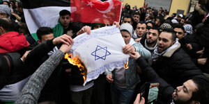 Eine Menschenmenge verbrennt eine Flagge mit einem Davidstern