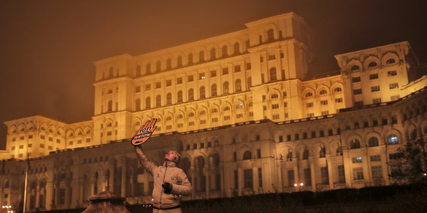 Mensch mit Papphand vor einem großen Gebäude