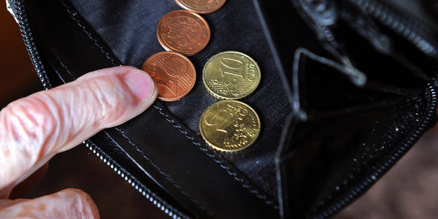 Eine alte Frau sieht in eine Geldbörse, in der sich nur wenige Cent befinden
