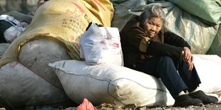 Eine alte Frau hockt am Rand eines Müllsackberges