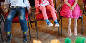 Beine von drei Kindern, die auf Stühlen sitzen