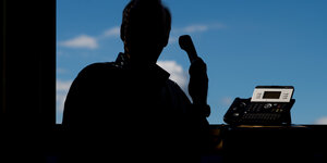 Ein Mann mit einem Hörer in der Hand vor einem Fenster, als Silhouette