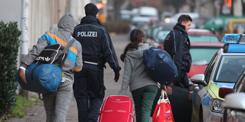 Polizisten geleiten Leute zu einem Fahrzeug