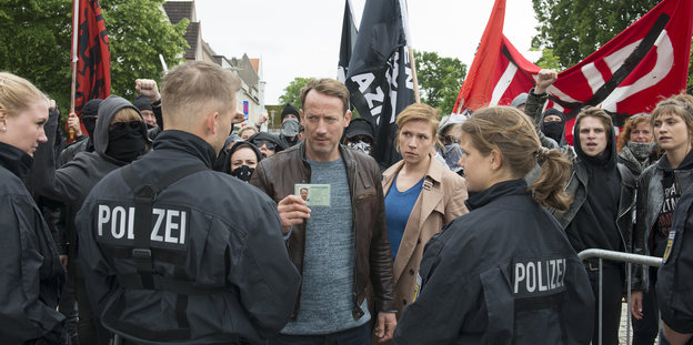 Demonstrant*innen mit schwarzer Kleidung und roten Flaggen stehen Polizist*innen gegenüber