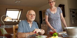 Ein Mann sitzt am Tisch, eine Frau steht daneben