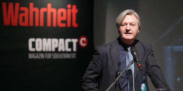 Ein Mann spricht vor schwarzem Hintergrund, auf dem "Wahrheit" und "Compact" steht Ein Mann spricht vor schwarzem Hintergrund, auf dem "Wahrheit" und "Compact" steht