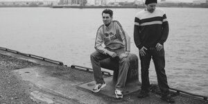Zwei junge Männer sitzen am Hamburger Hafen, es sind die Rapper Johnny Mauser und Captain Gips