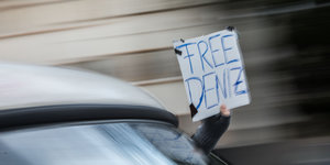 Aus einem fahrenden Auto hält jemand ein Schild mit der Aufschrift #Free Deniz