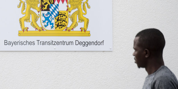 Ein Mann steht neben einem Schild auf dem steht: „Bayerisches Transitzentrum Deggendorf“