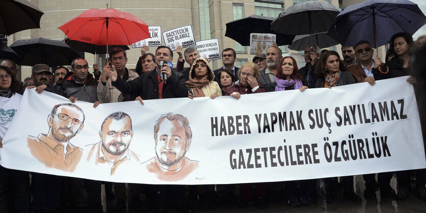 Mehrere Menschen stehen mit Regenschirm und Banner vor einem Gebäude