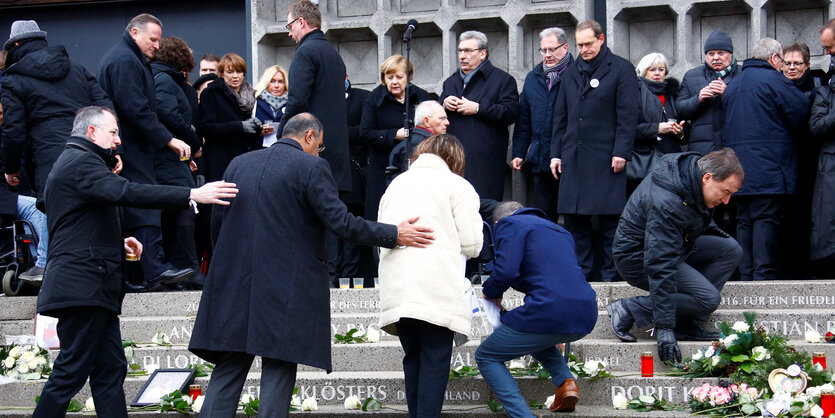 trauernde Menschen stehen vor einer Kirche, einige legen Kränze nieder