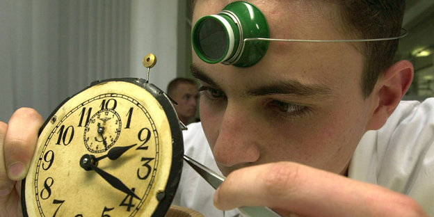 Ein junger Mann mit Stirnlampe repariert eine Uhr