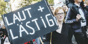 eine Frau hält ein Schild hoch, auf dem steht "Laut und Lästig"