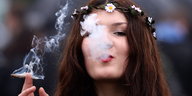 Eine junge Frau mit Blumenkette auf dem Kopf raucht einen Joint.