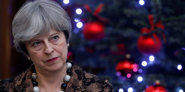 Theresa May blickt grimmig. Hinter ihr Weihnachtsbaumschmuck