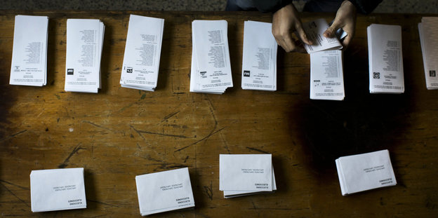 Eine Person steht am 21.12.2017 in einem Wahllokal in Barcelona vor Stapeln mit Wahlzetteln