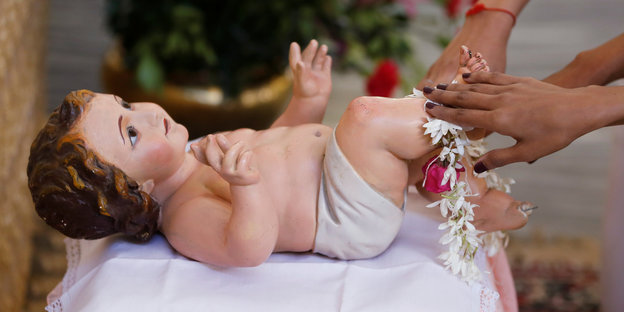eine Babyfigur wird von Frauenhänden berührt
