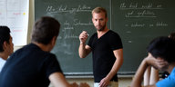 Ein Lehrer steht vor einer Klasse an der Tafel und erklärt seinen Schülern etwas
