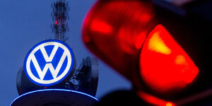 Ein großes Logo von Volkswagen leuchtet in der Dämmerung, davor ist eine rote Ampel zu sehen