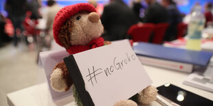 Ein Teddybär sitzt auf einem Tisch und hält das Schild „no Groko" auf seinem Schoß