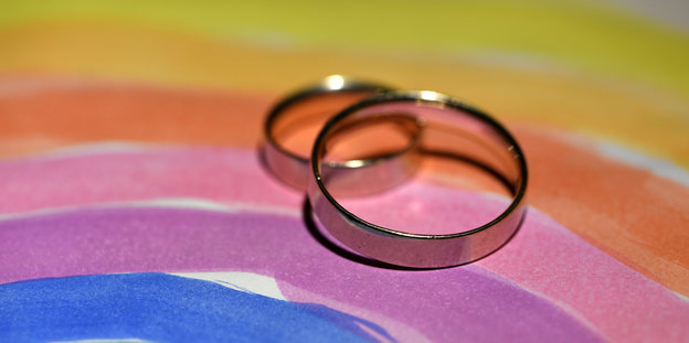 Zwei Ringe liegen auf einem Blatt Papier, auf dem ein Regenbogen gemalt ist.