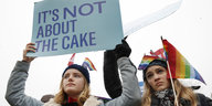 Zwei Demonstrantinnen, eine mit Regenbogenflagge, die andere hält ein Schild: "It's not about the cake"