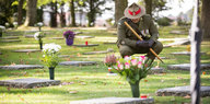 Ein Soldat in Uniform hockt vor einem Grab auf einem Friedhof